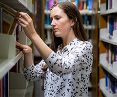 UCD student takes a book from a shelf.